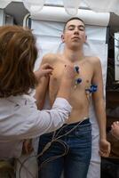 A female doctor performs an ECG on a young man in a hospital room, carefully monitoring his heart health during a routine checkup. photo