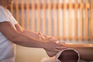 Foot Massage Therapy in a Relaxing Spa Setting. A professional massage therapist in a white uniform provides a soothing foot massage to a client in a calm and serene spa environment photo