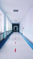 Motion along the corridor inside empty college. Blue long hallway with big windows in modern university. Vertical video