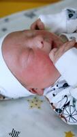 Gloved hands are fastening the buttons on baby's romper. Newborn kid starts to cry. Close up. Vertical video