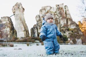 A baby in a blue snowsuit and hat is standing in soft snow photo