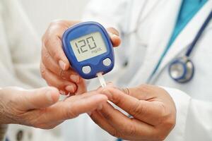 Asian doctor using digital glucose meter for check sample blood sugar level to treatment dia photo