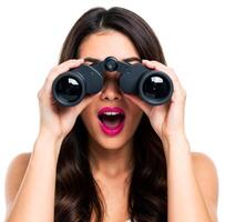 Attractive woman looking through binoculars with surprised expression and open mouth isolated on white background photo