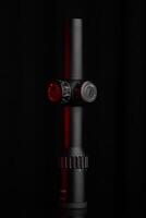 A stylish rifle scope in black with red accents, showcasing precision adjustment controls and magnification scales, against a deep, dark background. photo