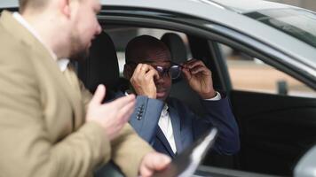 Car dealer and African American buyer discussing car features, creating positive sales experience. Happy customer learns about new car purchase from dealer in showroom. Sales concept. video