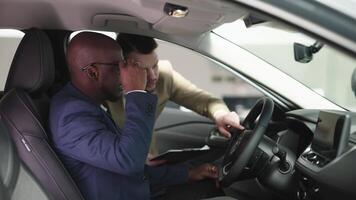 Caucasian car dealer and African American buyer discussing car features, creating positive sales experience. Happy customer learns about new car purchase from dealer in showroom video