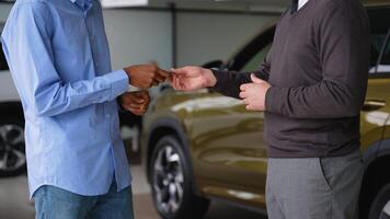 A car salesman hands over the keys to a customer while shaking hands at a dealership showroom video