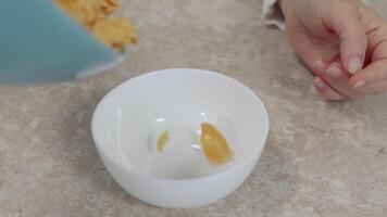 White ceramic bowl positioned on kitchen table while golden cornflakes cascading and filling surface, capturing dynamic stages of classic breakfast preparation moment video