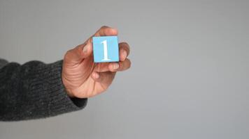 Hand holding a blue block with the number one in a neutral setting video