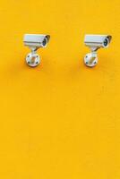 Two surveillance cameras mounted on a vibrant yellow wall, emphasizing security. photo