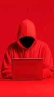 Mysterious figure in red hoodie using laptop in a minimalist setting. photo