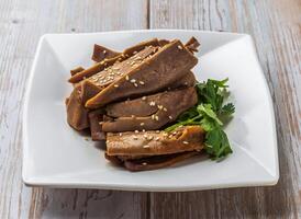 Spicy Sliced Pig Tongue with rich sauce, sesame seeds and cilantro served in plate on Wood Table Close up Side view of Hong Kong food photo