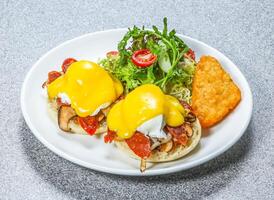 Eggs Benedict with two poached eggs with hollandaise sauce on English muffins, with salad and a hash brown served on a wooden board side view of hong kong food on a textured stone background photo