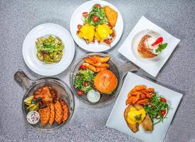 Kiwi Lamb Burger, Chicken Wings and Waffles, Shrimp pesto sauce pasta, Fried French Toast Cube, Fried Fish Benedict, and Eggs Benedict served isolated on stone background top view of hong kong food photo