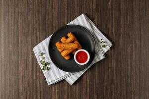 Deep fried crispy mozzarella cheese sticks with tomato dipping sauce isolated on wooden table top view photo
