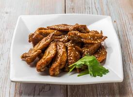 Honey Glazed Chicken Wing Tips with savory sauce, sesame seeds and cilantro served in plate on Wood Table Close up Side view of Hong Kong food photo