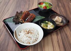 Unagi Bento, Grilled Eel, rice, miso soup, tofu, and a side salad served on black tray isolated on table side view of Japanese cousin photo