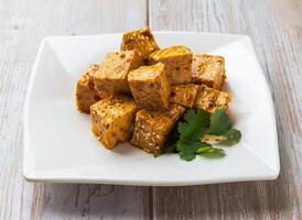 Spicy Marinated Tofu Cubes with savory sauce, sesame seeds and cilantro served in plate on Wood Table Close up Side view of Hong Kong food photo