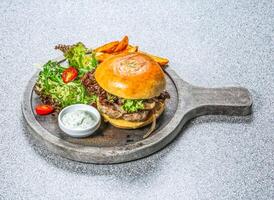 Kiwi Lamb Burger with brioche bun, juicy lamb patty, fresh salad, wedges, and tzatziki sauce served on a wooden board side view of hong kong food on a textured stone background photo