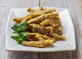 Braised chicken feet with savory sauce, sesame seeds and cilantro served in plate on Wood Table Close up Side view of Hong Kong food photo