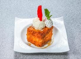 Fried French Toast Cube topped with ice cream, whipped cream, a mint sprig, and red candy served on a plate side view of hong kong food on a textured stone background photo