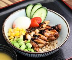 Teriyaki Chicken Don with egg and salad cucumber, corn, green peas, and tomato served in bowl isolated on table closeup side view of Japanese food photo