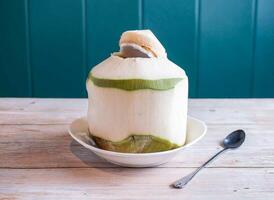 Fresh Coconut Drink in Shell with spoon served in plate isolated on wooden background top view of Hong Kong food photo