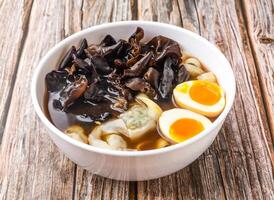 Hot Spring Egg Fungus Wonton Sliced Noodles Soup served in bowl isolated on wooden table side view of hong kong food photo