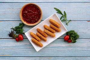 Deep fried crispy mozarella cheese sticks with tomato dipping sauce isolated on wooden table top view photo