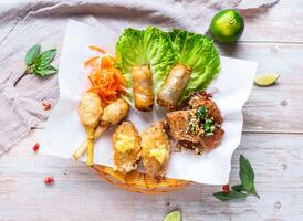 Vietnamese Appetizer Platter with Spring Rolls, fish cakes, and grilled pork, Grilled Shrimp satay and french butter chicken served in basket isolated on wooden background top view of Hong Kong food photo