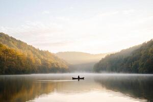 A man in a boat on a lake surrounded by trees photo
