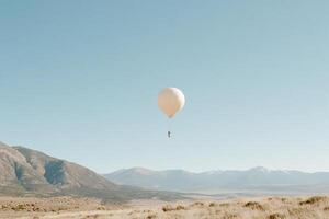 A white balloon flying over a field with mountains in the background photo
