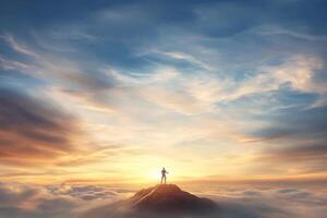 A man stands on top of a mountain with the sun setting behind him photo