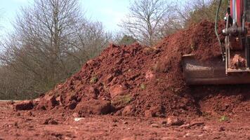 The excavator, equipped with a bucket, is raking clay soil mixed with stones. The heavy machinery is diligently working on the construction site, clearing the ground for upcoming building tasks video