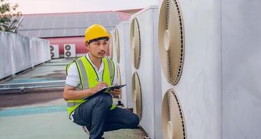 man in a yellow vest is writing on a clipboard while looking at an air conditioner photo