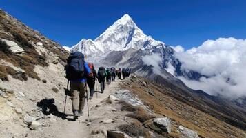 A group of hikers makes their way along a rugged mountain trail, surrounded by impressive snow-capped peaks under a bright blue sky. The trek appears challenging yet invigorating photo