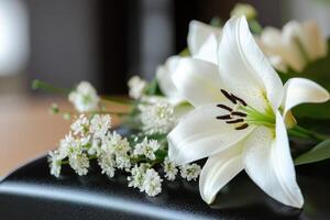 A combination of white lilies and small delicate flowers is thoughtfully placed on a dark surface, creating a poignant tribute at a funeral setting, symbolizing remembrance and peace photo