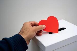 Hand Gently Dropping A Red Heart Into A Donation Box photo