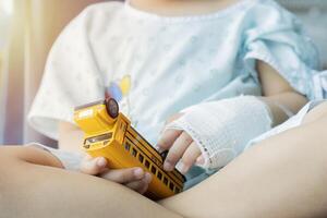 Sick kid in hospital with intravenous a saline on hand and holding a toy car while sitting in a chair photo