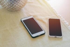 Two mobile phones on the dining room table with a tablecloth near by glass vase. photo