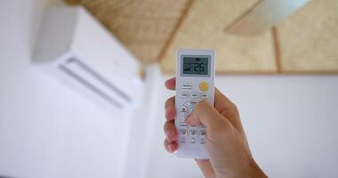 Hand uses remote activate air conditioner, lowering temperature button display comfort. effective against heat, ensuring cooler environment, welcome break intense summer heat. Heat relief action. video