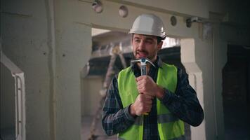 Cheerful active Caucasian man builder holding hammer working tool using as microphone singing song positive enjoy music male guy architect contractor engineer building construction repairman workman video