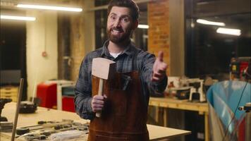 Joyful Caucasian carpenter wood master man wave hand come here gesture in workshop repairman architect recruitment craftsman male builder inviting worker holding wooden hammer guy welcoming sign smile video