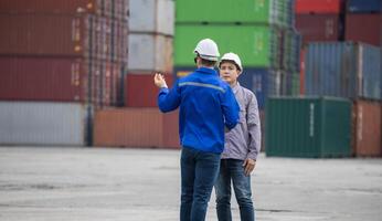 Supervisor in safety gear and engineer man checking and control loading containers box from shipping yard, Workers collaborating at shipping container cargo photo
