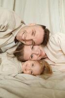Happy family posing closely together on a soft blanket in a cozy indoor setting during the day, with smiles and warmth shining through their expressions photo