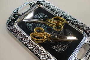Decorative silver tray showcasing golden-handled scissors resting on an intricately designed surface photo
