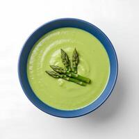 Green asparagus soup in blue ceramic plate, top view on white background with shadow. A creamy and nutritious soup made with fresh asparagus and herbs photo