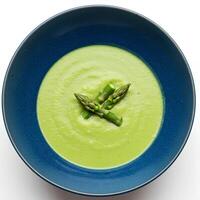 Green asparagus soup in blue ceramic plate, top view on white background with shadow. A creamy and nutritious soup made with fresh asparagus and herbs. Delicious asparagus soup in a blue plate photo