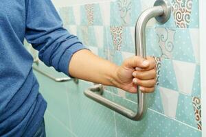 Asian woman patient use toilet support rail in bathroom, handrail safety grab bar, security in nursing hospital. photo