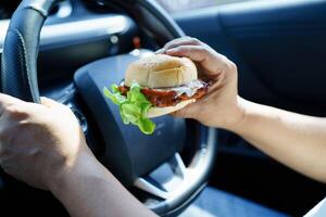 Asian woman driver hold and eat hamburger food in car. photo